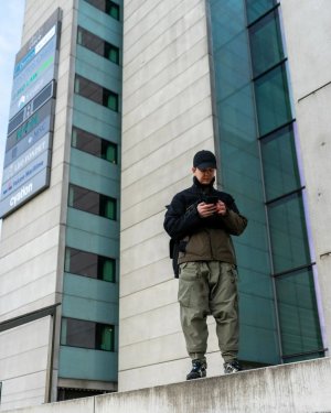 Techwear.Germany aka Janek neben einem großen futuristischen Gebäude in Kopenhagen in einem Techwear Outfit bestehend aus North Face Cap, ACRONYM J1WTS-GT Techwear Jacke, ACRONYM P30A-DS Techwear Hose, Equip Techwear Messenger Bag und Asics Gel Nimbus9 Schuhen