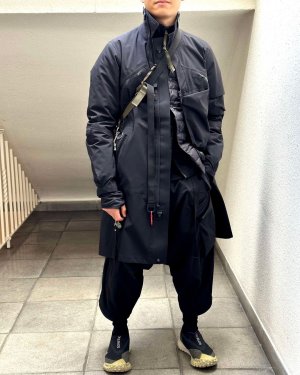 A man in a futuristic techwear outfit consisting of ACRONYM J1L-GT techwear coat, ACRONYM J97-M techwear jacket, ACRONYM P30A-E techwear pants and Nike Mountain Fly GTX techwear shoes