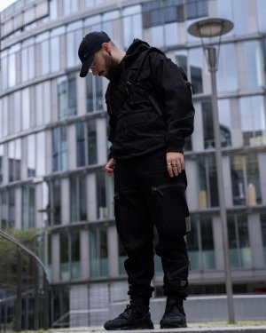 Ein Mann stehend vor einem futuristischen Gebäue in einem Techwear Outfit bestehend aus einem GStar Raw Overshirt, einer GStar Raw RCT Techwear Cargohose und Nike Air Huarache Techwear Schuhen