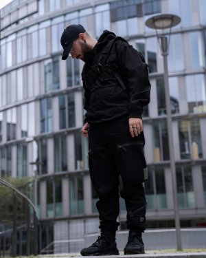 A man standing in front of a futuristic building in a techwear outfit consisting of a GStar Raw overshirt, GStar Raw RCT techwear cargo pants and Nike Air Huarache techwear shoes