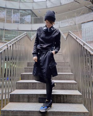 A woman on a staircase in a black techwear outfit consisting of Krakatau sweatshirt, Nike Jordan Future Primal Utility Skirt, Nike Runner Dry Leggings and Nke ISPA Drifter