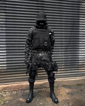 A man in an all-black warcore outfit with plate vest, magazine pouches, warcore pants with lots of accessories and mask
